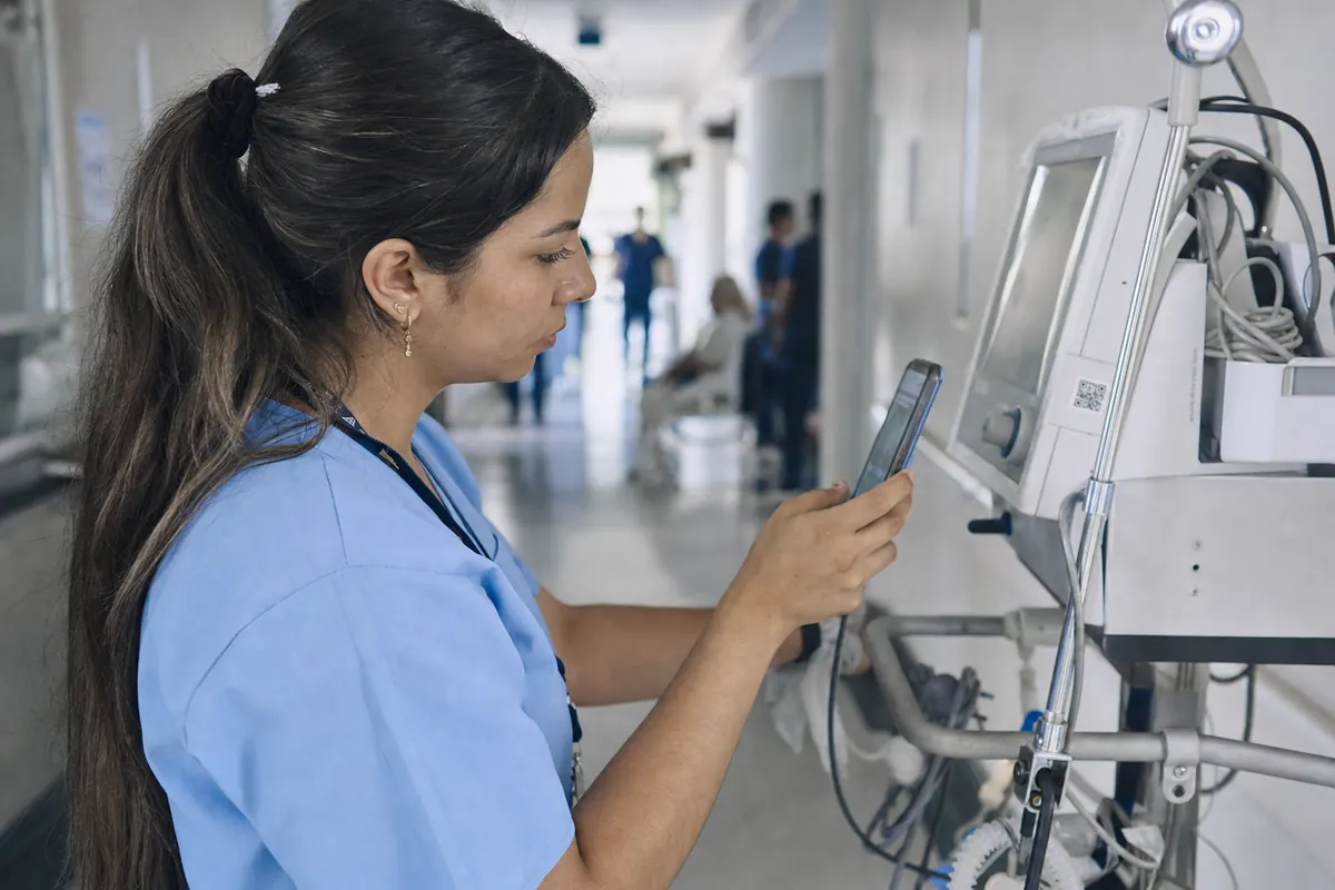 Biomedical engineer scans the QR code on a ventilator with her phone in a hospital corridor