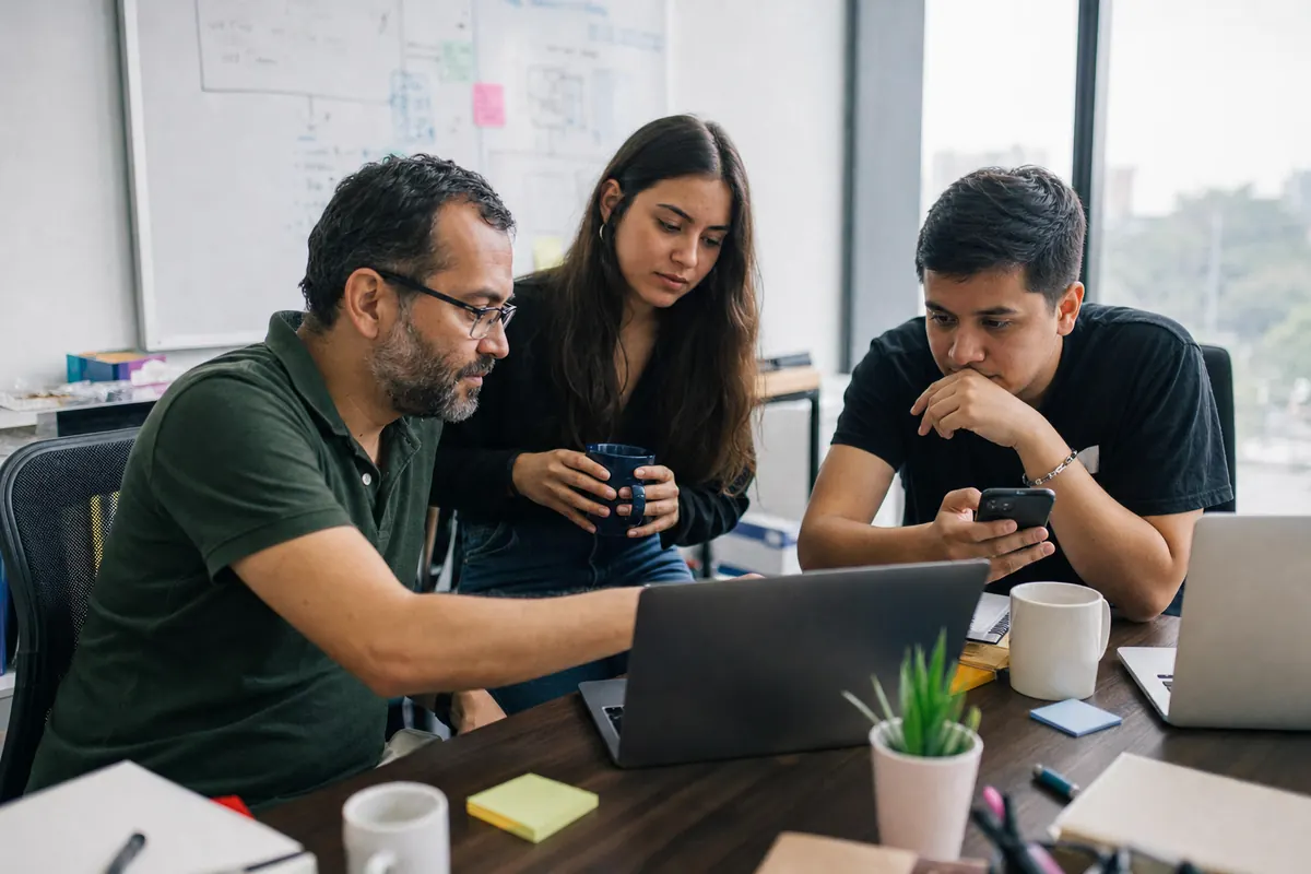Three members of a software team review a request together on a laptop and a phone