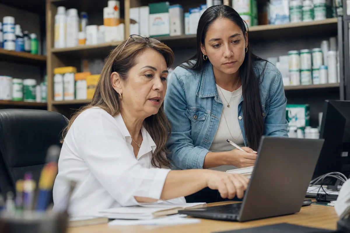 Owner of a distribution company and her assistant review a software demo on a laptop